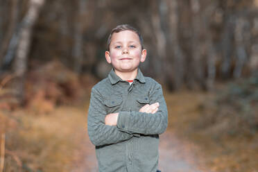 Boy with arms crossed standing in park during autumn - WPEF03562