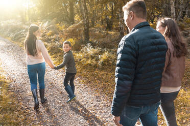 Geschwister schauen über die Schulter auf ihre Eltern, die im Herbst im Park spazieren gehen - WPEF03568