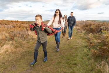 Children holding scarf while parents walking behind in park during autumn - WPEF03572