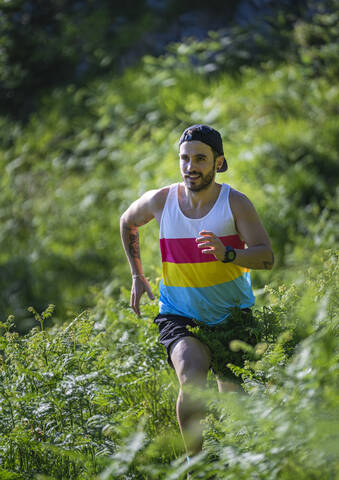 Sportsman looking away while running between grass on mountain at forest stock photo