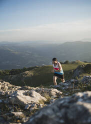 Man running on mountain trail against mountain range and clear sky - SNF00773