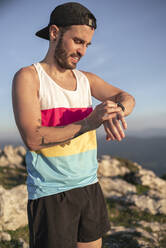 Athlete checking time while standing on mountain against clear sky - SNF00775
