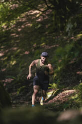 Männlicher Sportler läuft auf einem Bergpfad im Wald - SNF00784