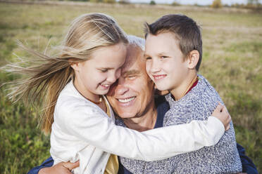 Lächelnder Großvater umarmt Enkelkinder auf dem Feld - EYAF01383