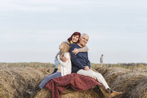 Granddaughter with grandparents on hay bale against sky during weekend stock photo