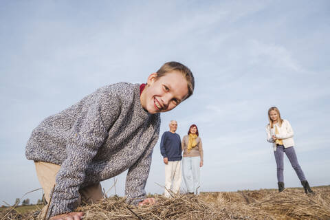 Happy boy crouching at hay bale while family in background stock photo