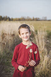 Lächelnder niedlicher kleiner Junge mit Blume auf einem Feld stehend - EYAF01405