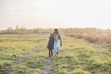 Ältere Frau geht mit ihrer Enkelin an einem sonnigen Tag auf einem Feld spazieren - EYAF01414