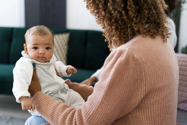 Mutter hält ihre kleine Tochter, während sie zu Hause sitzt - GIOF09501