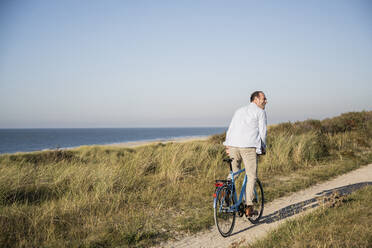 Glücklicher Mann fährt Fahrrad am Strand gegen den klaren Himmel - UUF21975