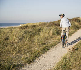 Glücklicher Mann betrachtet die Aussicht beim Fahrradfahren am Strand gegen den klaren Himmel - UUF21977