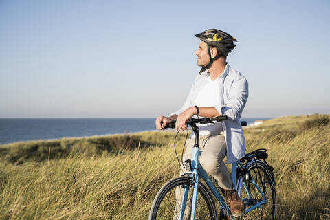Man looking at view while sitting on bicycle by grassy field against clear sky stock photo