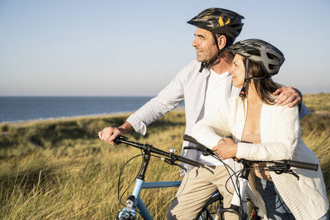 Smiling mature couple looking at view while standing with bicycles at beach stock photo