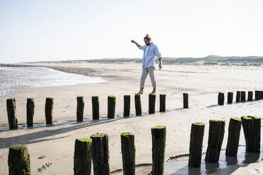 Junger Mann läuft auf Holzpfählen am Strand gegen den klaren Himmel - UUF21994