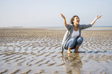 Playful young woman throwing water at seashore - UUF22011