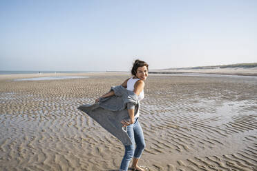 Carefree young woman at beach against clear sky on sunny day - UUF22013