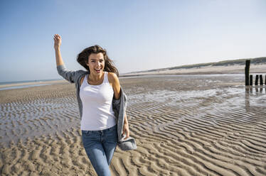 Glückliche junge Frau, die an einem sonnigen Tag am Strand spazieren geht - UUF22018