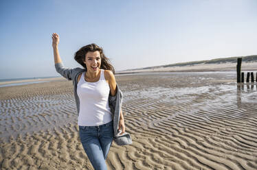 Happy young woman walking at beach during sunny day - UUF22018