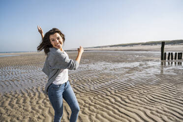 Playful young woman spinning at beach against clear sky during sunny day - UUF22019