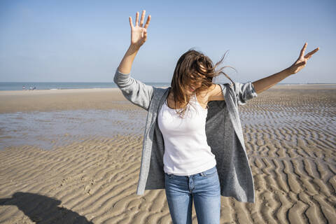 Happy young woman dancing at beach against clear sky during sunny day stock photo