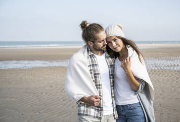 Young couple covered in blanket spending leisure time at beach during weekend - UUF22023