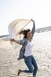 Fröhliche Frau läuft mit Decke am Strand an einem sonnigen Tag - UUF22036