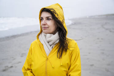 Contemplated mature woman in yellow raincoat at beach during weekend - UUF22044