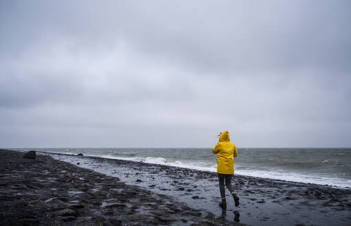 Woman walking at sea shore against cloudy sky - UUF22047