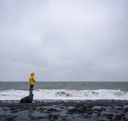 Frau steht auf einem Felsen am Meeresufer vor bewölktem Himmel - UUF22051