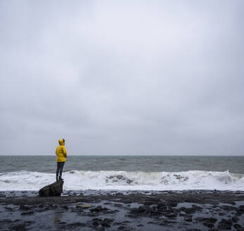 Woman standing on rock at sea shore against cloudy sky - UUF22051