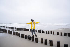 Frau geht auf Holzpfählen am Strand gegen den Himmel - UUF22053