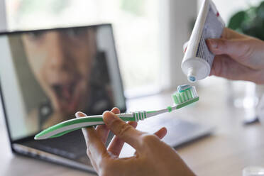 Hands of female dentist applying paste on toothbrush showing through video call to patient - AFVF07422