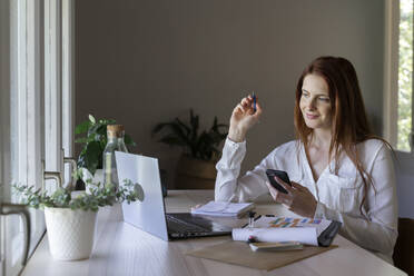 Lächelnde Frau, die ein Handy und einen Fidget Spinner benutzt, während sie zu Hause sitzt - AFVF07427