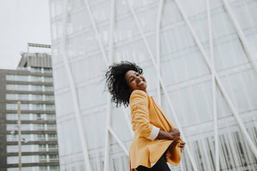 Smiling female entrepreneur with eyes closed standing against office building - GMLF00762