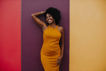 Smiling woman with hand in hair standing against colorful wall - GMLF00771