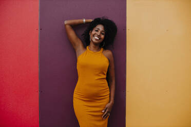 Happy woman with hand in hair standing against colorful wall - GMLF00772