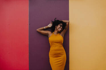 Carefree woman with hand in hair standing against colorful wall - GMLF00775