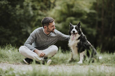 Mann schaut Hund an, während er auf dem Fußweg an einer öffentlichen Arche sitzt - GMLF00784