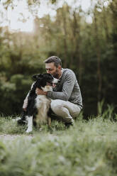 Man kissing his dog while crouching at park - GMLF00785