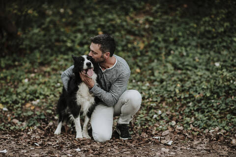 Mature man kissing his dog while sitting at park stock photo