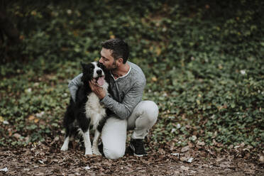 Mature man kissing his dog while sitting at park - GMLF00788
