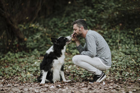 Mann spielt mit Hund, während er sich in einem öffentlichen Park duckt - GMLF00789