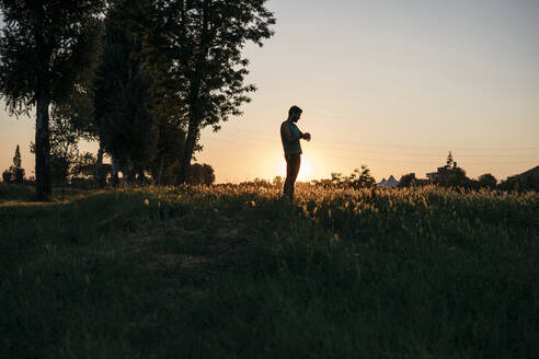 Sportler, der während des Sonnenuntergangs im Park im Gras steht - SBAF00047