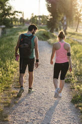Aktives Paar in Sportkleidung beim Spaziergang im Park während des Sonnenuntergangs - SBAF00050