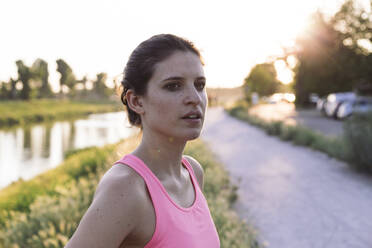 Confident sportswoman looking away while standing in park during sunset - SBAF00051