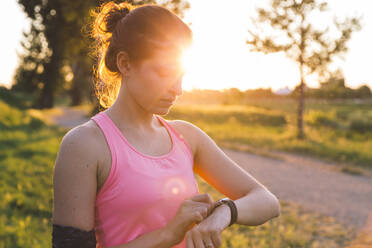 Junge Sportlerin, die im Park stehend die Zeit auf einer intelligenten Uhr überprüft - SBAF00053