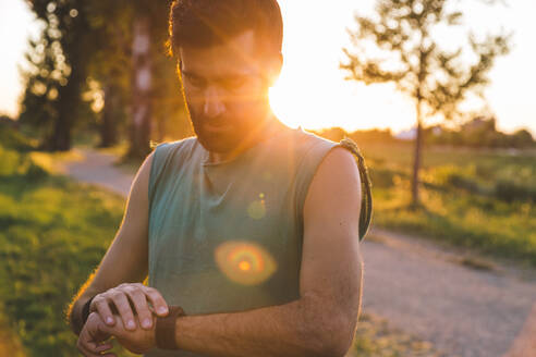 Junger Sportler, der im Park stehend die Zeit auf seiner Smartwatch überprüft - SBAF00054
