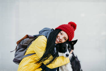 Happy woman embracing pet dog against wall - EBBF01206