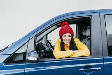 Lächelnde Frau mit verschränkten Armen, die während einer Autoreise durch das Autofenster schaut - EBBF01240