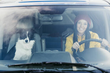 Lächelnde Frau mit Hund, gesehen durch die Windschutzscheibe eines Autos während einer Autofahrt - EBBF01242